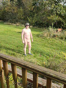 Naked human standing outdoors in naturist setting, embracing natural body expression.