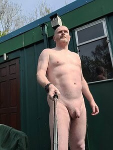 Naturist nudist nude naked penis, standing outdoors, holding selfie stick, confident pose.