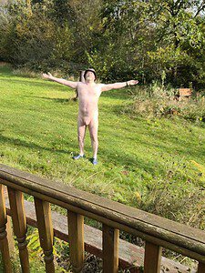 Naturist nudist nude naked penis standing outdoors with arms open in nature.