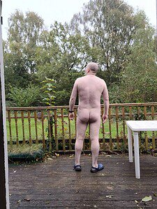 Naturist nudist nude naked penis male standing outdoors on wooden deck.