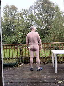 Naturist nudist nude naked penis man standing outdoors on a wooden deck.