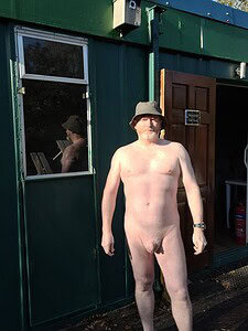 Nudist man standing outdoors with a green background and a hat.