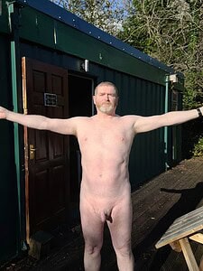 Naturist nudist nude naked penis man standing outdoors with arms outstretched.