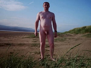 Naturist nudist nude naked penis man standing outdoors on a beach.