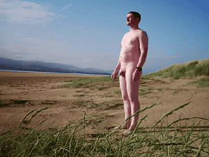 Naturist nudist nude naked penis man standing on beach with blue sky.