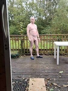 Naturist nudist nude naked penis man standing outdoors on a deck.