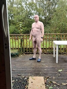Naturist nudist nude naked penis man standing outdoors on wooden deck.