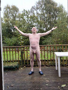 Naturist nudist nude naked penis man standing outdoors with arms open.