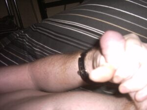 A close-up of a forearm with light skin tone resting on a striped bedspread. The wrist is adorned with a black watch, and the hand is positioned in a relaxed grip. The background shows a part of the bedding with linear stripes, contributing to a serene indoor atmosphere.