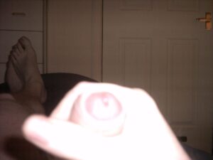 The image depicts a close-up of a hand holding a small object, with blurred feet in the background resting on a soft surface. The surroundings appear dimly lit, creating a soft contrast with the hand and the object, which seems to be a small, round item.