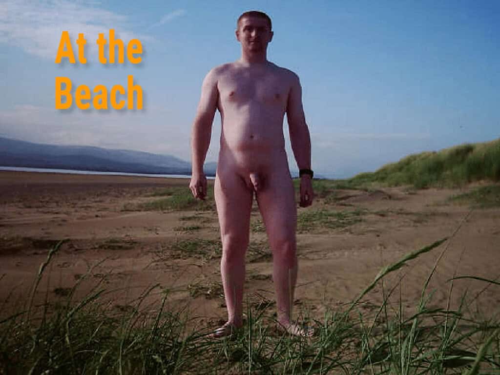 Nude man standing on the beach with sand and grass, scenic coastal background.