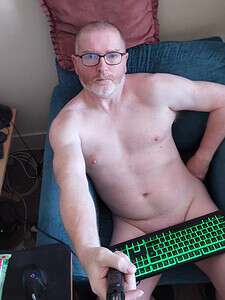Naturist nudist nude naked penis, man sitting on sofa, relaxed pose, natural setting.