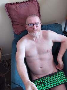 Naturist nudist nude naked penis man with glasses sitting on bed.