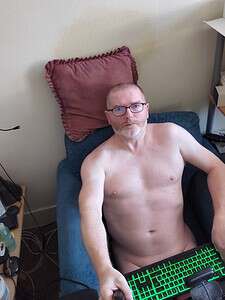 Naturist nudist nude naked penis man relaxing on sofa with glasses.