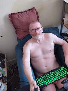 Naturist nudist nude naked penis man sitting on bed with keyboard in hand.