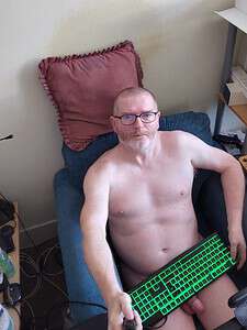 Naturist nudist nude naked penis man sitting on sofa with keyboard in hand.