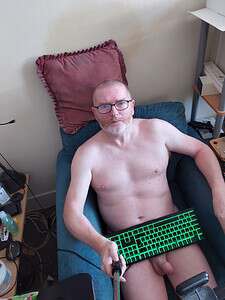 Naturist nudist nude naked penis man sitting on sofa with keyboard in hand.