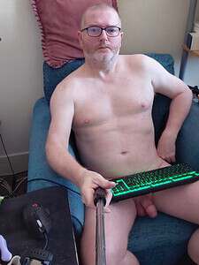 Naturist nudist nude naked penis man sitting on sofa with keyboard and selfie stick.