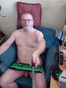Naturist nudist nude naked penis, man sitting on sofa with gaming keyboard and selfie stick.
